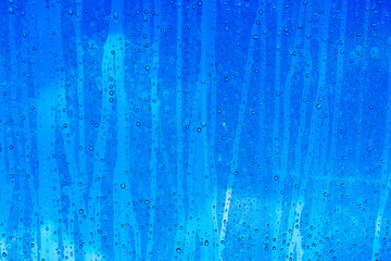 Regentropfen auf Glasscheibe mit blauem Hintergrund