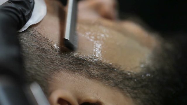Master makes a haircut beard client with straight razor