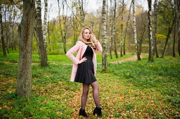 Young blonde girl at pink coat posed on autumn park.