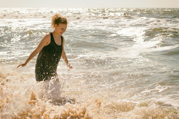 Young girl stands in waves at sea on a clear sunny day