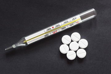 thermometer with temperature next to pills, close up