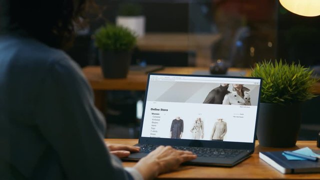 Woman Sitting at Her Desk with the Laptop Looks at Online Retail Clothing Store Website. Site Shows Various Male and Female Stylish Clothes, New Collection. RED EPIC-W 8K Camera.