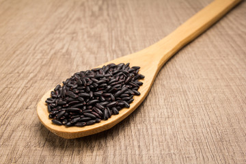 Black Rice seed. Spoon and grains over wooden table.