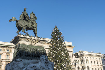 Fototapeta na wymiar Vittorio Emanuele II statue in Duomo square in Milan, Italy, with Christmas tree in a sunny day of december.