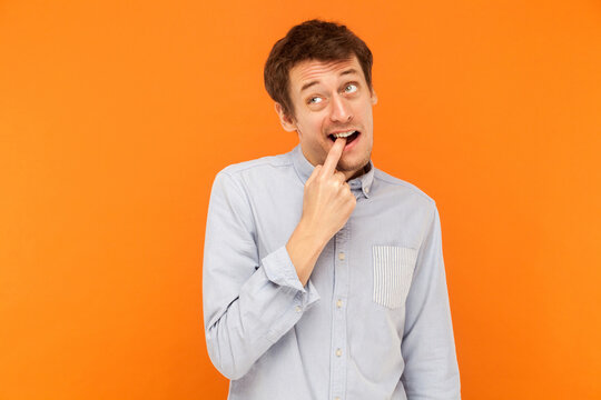 Something is stuck between teeth. Funny young adult business man touching finger teeth and looking up