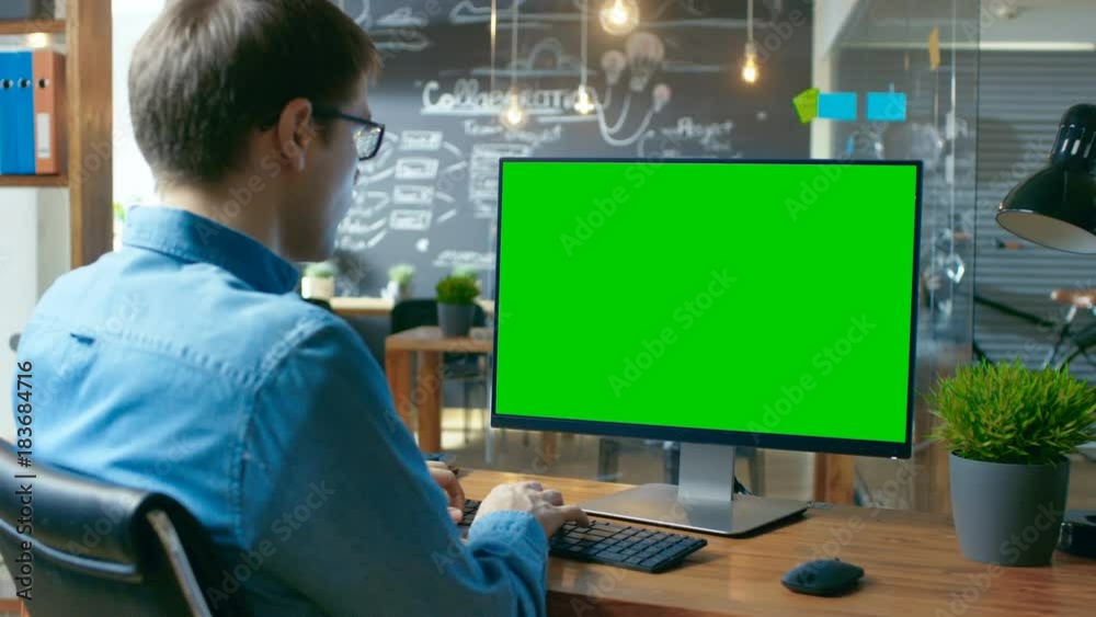 Poster young man works at his desk on the personal computer with mock-up green screen. in the background hi