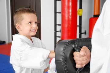 Male karate instructor training little boy in dojo