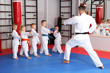 Male karate instructor training little children in dojo - obrazy, fototapety, plakaty