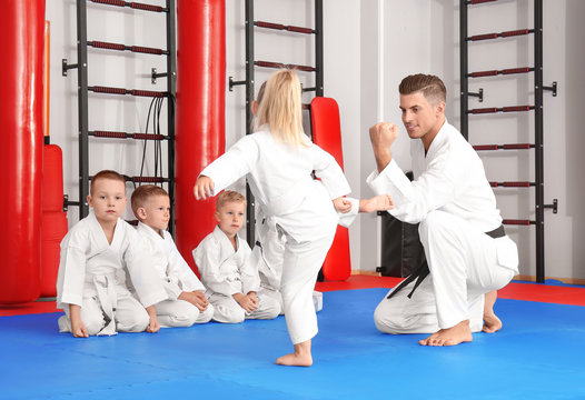 Male karate instructor training little children in dojo