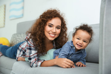 Cute baby and young mother lying on sofa at home