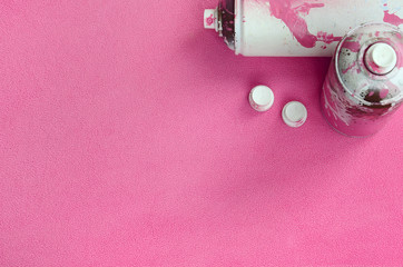 Some used pink aerosol spray cans and nozzles with paint drips lies on a blanket of soft and furry...