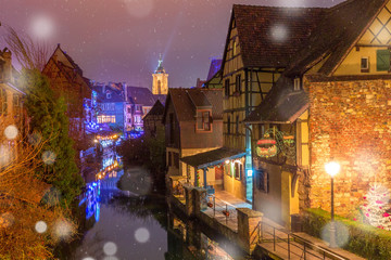 Traditional Alsatian half-timbered houses, church and river Lauch in Petite Venise or little Venice, old town of Colmar, decorated and illuminated at snowy christmas night, Alsace, France