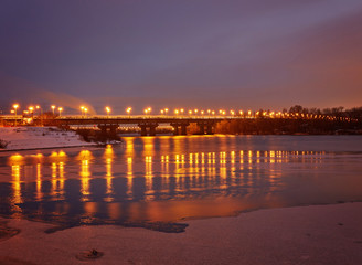 Fototapeta na wymiar Bridge on the River Dnieper in the evening. Lantern light is reflected in the frozen ice, city
