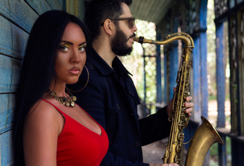 Young beautiful girl singer  with saxophone players on old house background. musical duet 