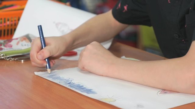 Close-up of unknown little girl draws the pictures using color pencils in the album in the kindergarten