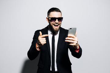 Portrait of a cheerful happy man in suit and tie read sms on phone and smile isolated over gray background