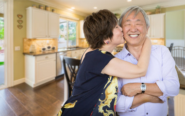 Happy Senior Chinese Couple Kissing Inside Beautiful Custom Kitchen.