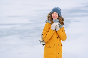 Beautiful smiling girl in a yellow winter jacket with skates in the middle of a frozen lake.