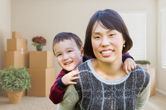 Chinese Mother and Mixed Race Child Inside Empty Room with Moving Boxes and Plants.