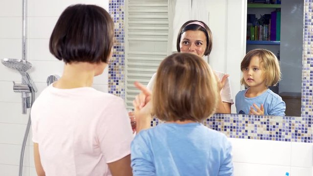 Little blond girl applying beauty mask on face of mother in bathroom tracking shot