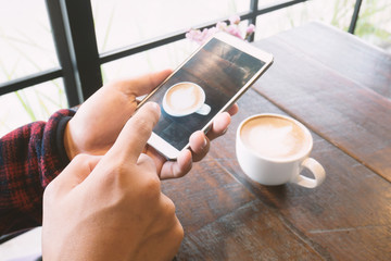 Hand holding smartphone and take a photo of coffee in the coffee shop
