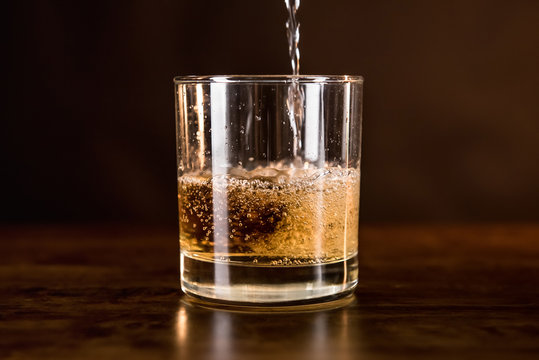 Whisky drink being poured in into the glass on wooden counter bar