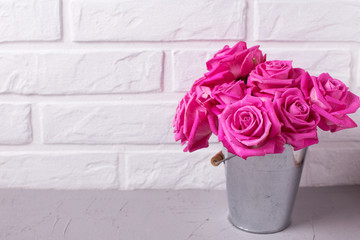 Bright pink roses flowers in bucket on grey background against white wall.