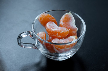 Tangerine slices in a transparent mug on a black background