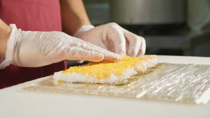 Professional sushi chef preparing roll at commercial kitchen, close-up.