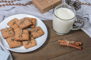 A cup of milk, cinnamon sticks and homemade cookies in a Christmas decor.