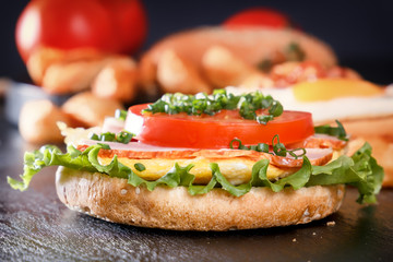 Sandwich with fried egg, bacon, tomato, greens. Breakfast with fried potatoes and mushrooms. Black background