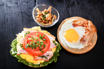 Fried egg on a roll. Sandwich with bacon, tomato and vegetables. Mushrooms. Breakfast. Black background
