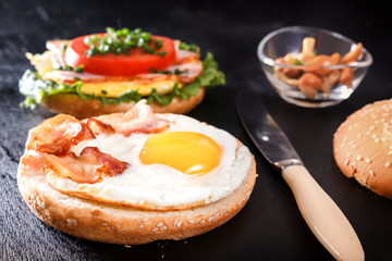 Breakfast with fried egg on bread, bacon, mushrooms, tomatoes and greens. Black background