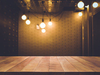Wood table top on blurred of counter cafe shop with light bulb background.