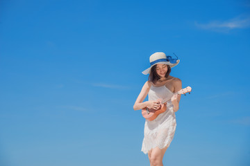 Cute young woman playing akulele on the sea beach with happy smiling on the face at daylight sunny,  cleared blue sky