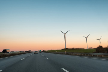 Multi-lane expressway at sunset. Highway. Three wind power plant generators are to the right of the road.