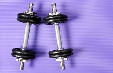 Black dumbbell on purple fitness mat. Exercise equipment. Healthy lifestyle concept.