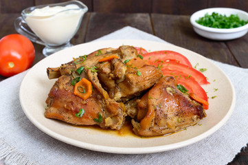 Stewed rabbit pieces with fresh tomato on a ceramic plate on a dark wooden background. Dietary menu.