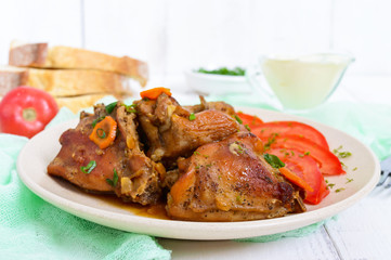 Pieces of rabbit with tomato, sauce and greens on a white wooden background