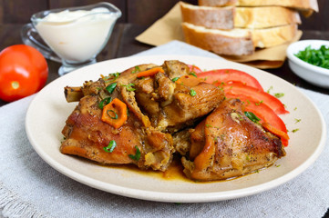 Stewed rabbit pieces with fresh tomato on a ceramic plate on a dark wooden background. Dietary menu.