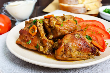 Stewed rabbit pieces with fresh tomato on a ceramic plate on a dark wooden background. Dietary menu.