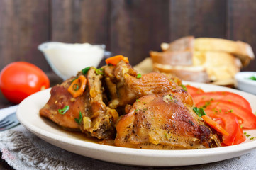 Stewed rabbit pieces with fresh tomato on a ceramic plate on a dark wooden background. Dietary menu. Close up