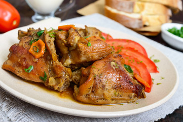 Stewed rabbit pieces with fresh tomato on a ceramic plate on a dark wooden background. Dietary menu. Close up