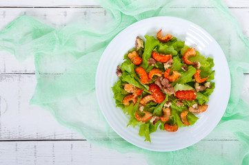 Light dietary spicy salad of lettuce, seafood (crawfish, shrimp) and walnuts on a white wooden background. Top view. Proper nutrition