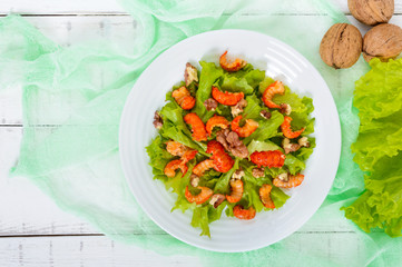 Light dietary spicy salad of lettuce, seafood (crawfish, shrimp) and walnuts on a white wooden background. Top view. Proper nutrition