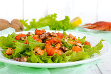 Light dietary spicy salad of lettuce, seafood (crawfish, shrimp) and walnuts on a white wooden background. Proper nutrition