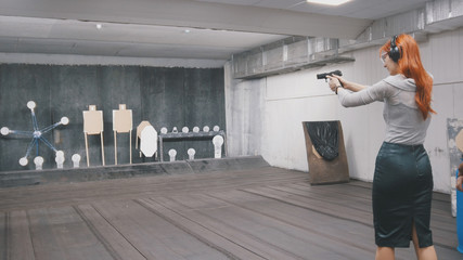 Woman with red hair shooting with a gun in shooting gallery
