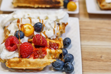 belgian waffle with raspberries and blueberries on wood table.