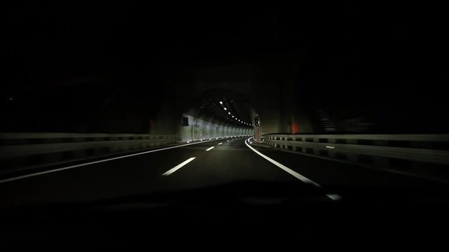 Car traveling on the A2 freeway on a rainy night in and out of tunnel in Leventina vallaey, Ticino 