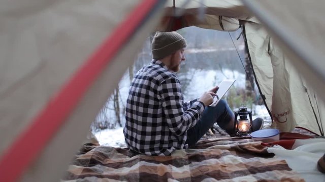man with a tablet in a tent on the shore of a winter lake